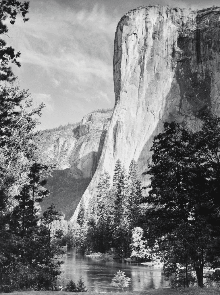 a large rock cliff with trees and a river